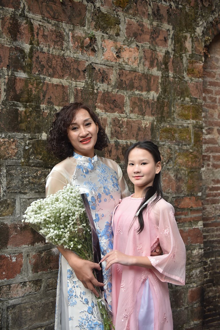 A mother and daughter pose with a bouquet against a rustic brick wall.