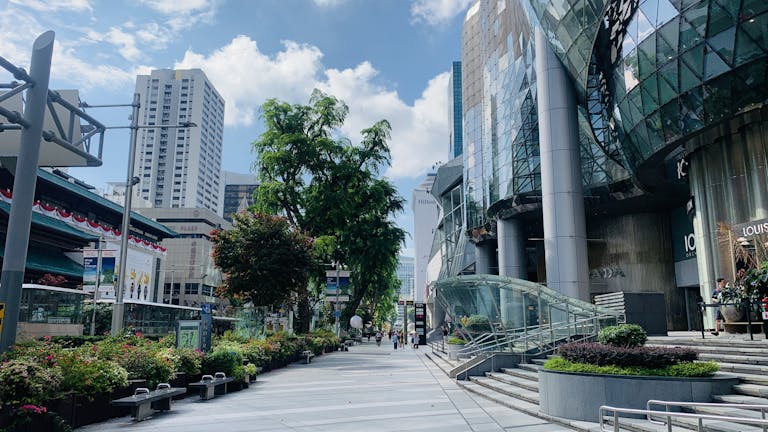 A vibrant street in Singapore featuring modern skyscrapers, lush greenery, and clear blue skies.